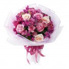 Bouquet of purple and cream roses with pink carnations, wrapped in white paper and tied with a pink ribbon.