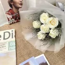 A bouquet of white roses wrapped in sheer white paper, with magazines and photos.