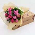 Pink lotus flowers in a bouquet wrapped in sheer gold fabric on a cardboard box.