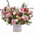 A large floral arrangement in a lilac box with roses, chrysanthemums, and greenery.