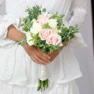 Bride holding a pastel pink and white rose bouquet with greenery.