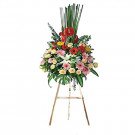 A large, vibrant flower arrangement with red, pink, yellow, and white flowers on a wooden easel.
