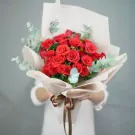 A bouquet of red roses with eucalyptus, wrapped in cream paper and tied with a brown ribbon.