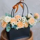 Basket of light orange and white roses with daisies and eucalyptus, tied with a ribbon.