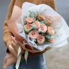Peach roses bouquet wrapped in brown and white paper with a ribbon.