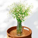 Bunch of chamomile flowers in a clear vase on a rattan tray.