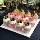 Assortment of cupcakes with cream, berries, chocolate, and walnuts on a white tray.