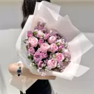 Pink and purple roses arranged in a bouquet, held by a person wearing a watch.