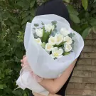 Bouquet of white tulips with greenery, wrapped in white paper and tied with a pink ribbon, held by a person.