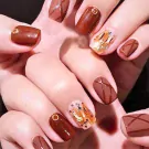 Close-up of a woman's hands with chocolate brown gel nails, some with a criss-cross design and others with gold accents.