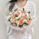 A woman holds a bouquet of pink and white roses and other flowers, wrapped in cellophane.