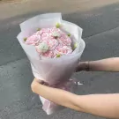Pink rose bouquet with small white flowers, held by two hands with a gold watch on one wrist.