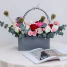 Floral arrangement in a gray box with white and pink roses, red carnations, and eucalyptus.