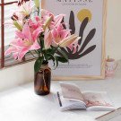 Pink lilies in a brown vase with a book and Matisse print.