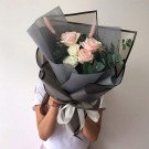 Bouquet of pink and white roses with eucalyptus in dark grey paper, tied with a white ribbon.
