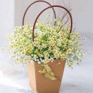 Basket of white and yellow chamomile flowers with baby's breath in a brown paper bag.