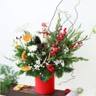 Christmas arrangement with a snowman, red berries, pinecones, dried orange slices, and greenery in a red vase.
