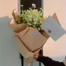 Bouquet of daisies with an envelope, presented by a hand.