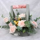 Pink roses and gold chocolate candies in a grey flower basket with pink ribbon handle.