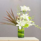 White lilies, orchids, and anthurium in a green striped glass vase.