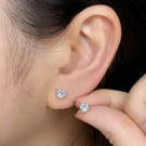 Close-up of a woman's ear with two small, clear, heart-shaped blue topaz stud earrings.