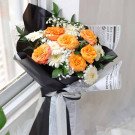 Orange roses and white gerbera daisies in a bouquet wrapped in black and newspaper-style paper.