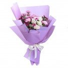 Bouquet of white roses, pink carnations, and purple chrysanthemums wrapped in purple paper.