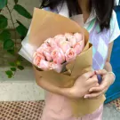 A bouquet of 22 pink roses wrapped in brown paper, held by a person wearing a sweater vest.