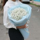 A woman in a white blouse holds a bouquet of white baby's breath flowers wrapped in light blue paper.