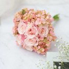 Pink roses and hydrangeas in a bridal bouquet on a marble surface.