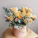 A pink hatbox arrangement of yellow and pink roses with baby's breath and eucalyptus.
