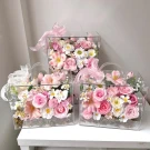 Clear boxes filled with pink and white artificial flowers, decorated with pink bows.