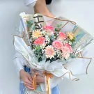 A bouquet of pink roses and orange gerbera daisies wrapped in newspaper and white paper.