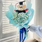 Graduation bouquet with a teddy bear wearing a cap and gown, surrounded by baby's breath flowers.
