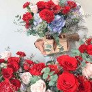 A wooden box filled with red roses, red carnations, and blue hydrangeas.