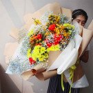 Bright bouquet of yellow, red, and orange flowers with baby's breath and greenery.