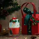 Christmas candle in a glass, decorated like a festive drink, with a red gift box and ribbon.