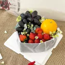 Fruit box with grapes, strawberries, and an orange, decorated with flowers and greenery.