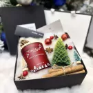 Christmas gift box with red scented candle, green Christmas tree candle, cinnamon sticks, and festive decorations.