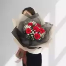 A bouquet of red roses with baby's breath, wrapped in black and beige paper, held by a person.