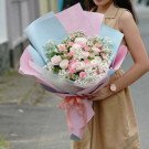 Woman holding a pink and white rose and carnation bouquet wrapped in blue and pink paper.