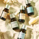 Five amber glass essential oil bottles with silver caps on sand, each with a distinct label.