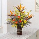 A tropical flower arrangement in a striped vase featuring Bird of Paradise and yellow orchids.