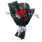 Red roses wrapped in black paper with eucalyptus and a silver ribbon.