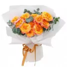 Bouquet of orange and pink roses with eucalyptus, wrapped in white paper and tied with a gold ribbon.