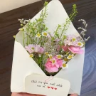 A bouquet of pink and white flowers in a cream envelope, with a handwritten card.