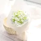A delicate bouquet of white and green hydrangeas wrapped in white paper, resting in a wicker basket.
