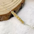 Silver bracelet with raw yellow gemstone bar pendant on a wooden surface.