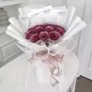 Amethyst Pink bouquet with deep pink roses, white wrapping, and a pink ribbon.