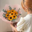 Woman holding a bouquet of sunflowers, baby's breath, and eucalyptus, wrapped in pink paper.